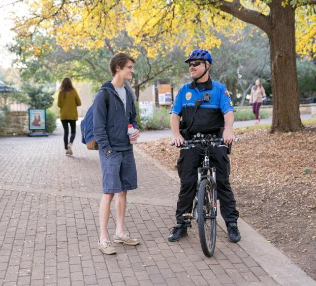 一名大学警察坐在自行车上和一名学生交谈，其他学生走在他们后面.